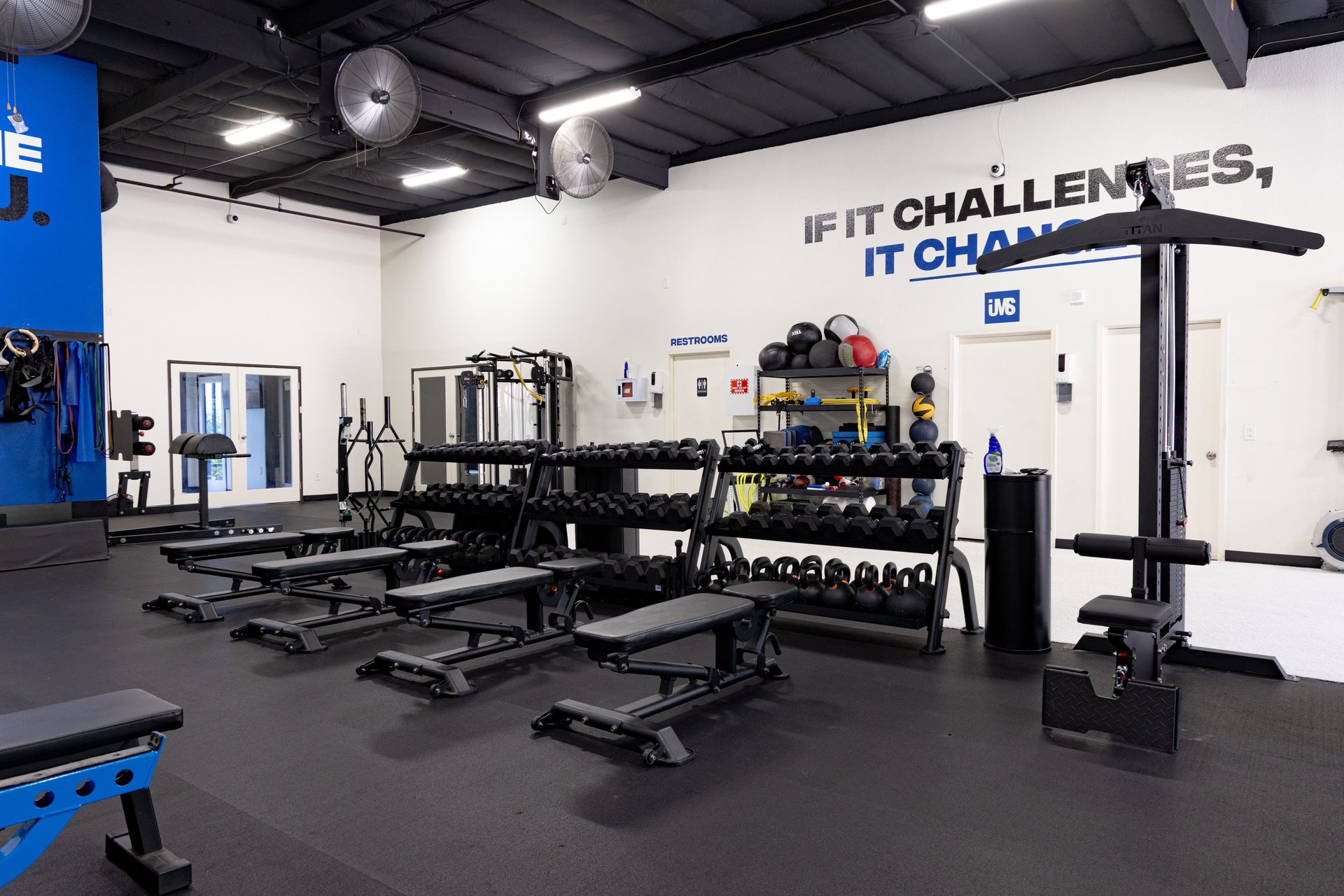 Dumbbell racks and benches beneath the If It Challenges wall at IMS