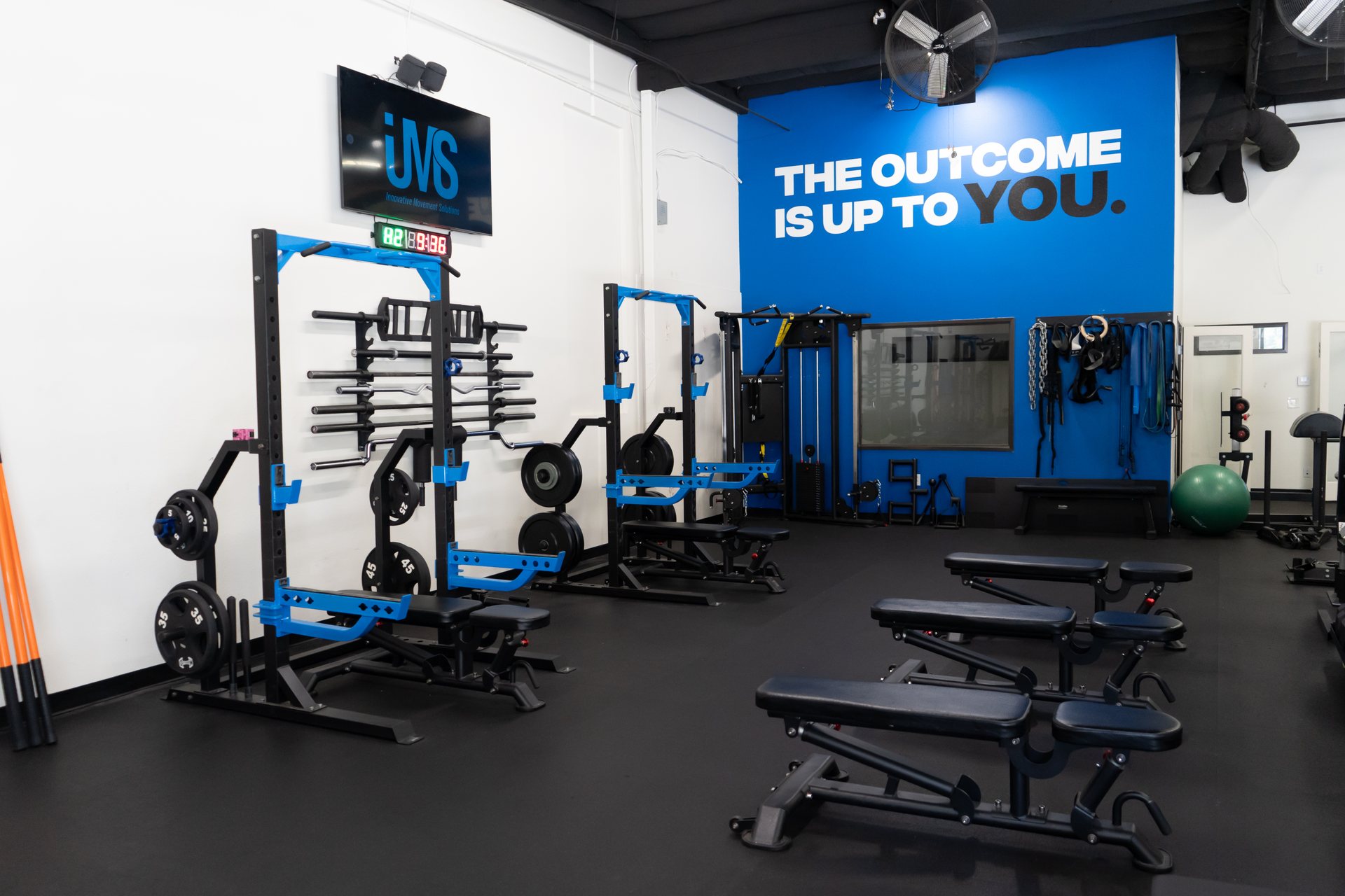 Squat racks and benches beneath the Outcome Is Up To You wall at IMS